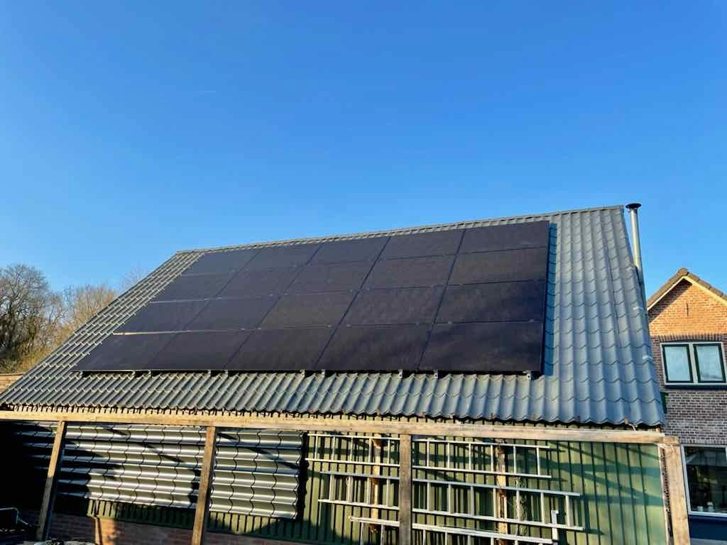 schuurdak met zwarte zonnepanelen tegen een strakblauwe lucht